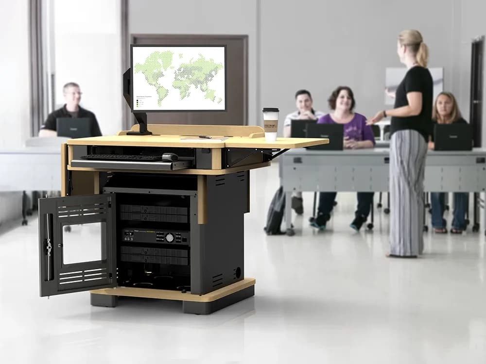 Instructor presenting in classroom using wood lectern with AV equipment and monitor